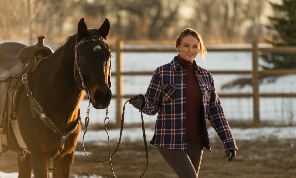 Woman in warm clothing walking a horse, showcasing best base layers for farm work in cold weather