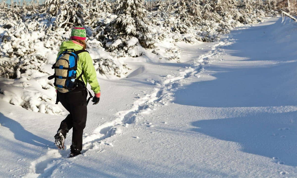 Person hiking in winter gear on a snowy trail, showcasing cold weather hiking essentials for adventure