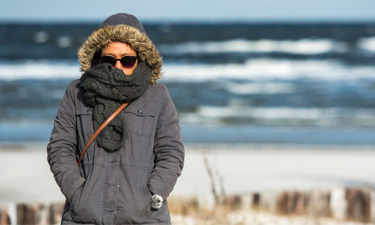 Person in warm winter clothing demonstrating which body parts need protection from cold at the beach