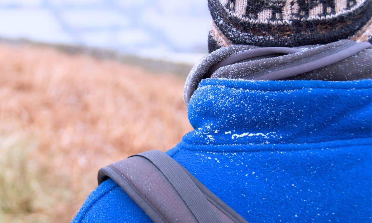 Person wearing a blue fleece jacket showing the benefits of fleece in cold weather with snowflakes on the fabric