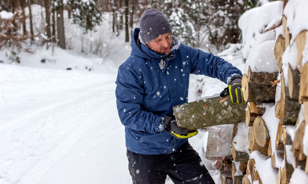 Man stacking firewood in snow while wearing best base layers for outdoor work in winter conditions