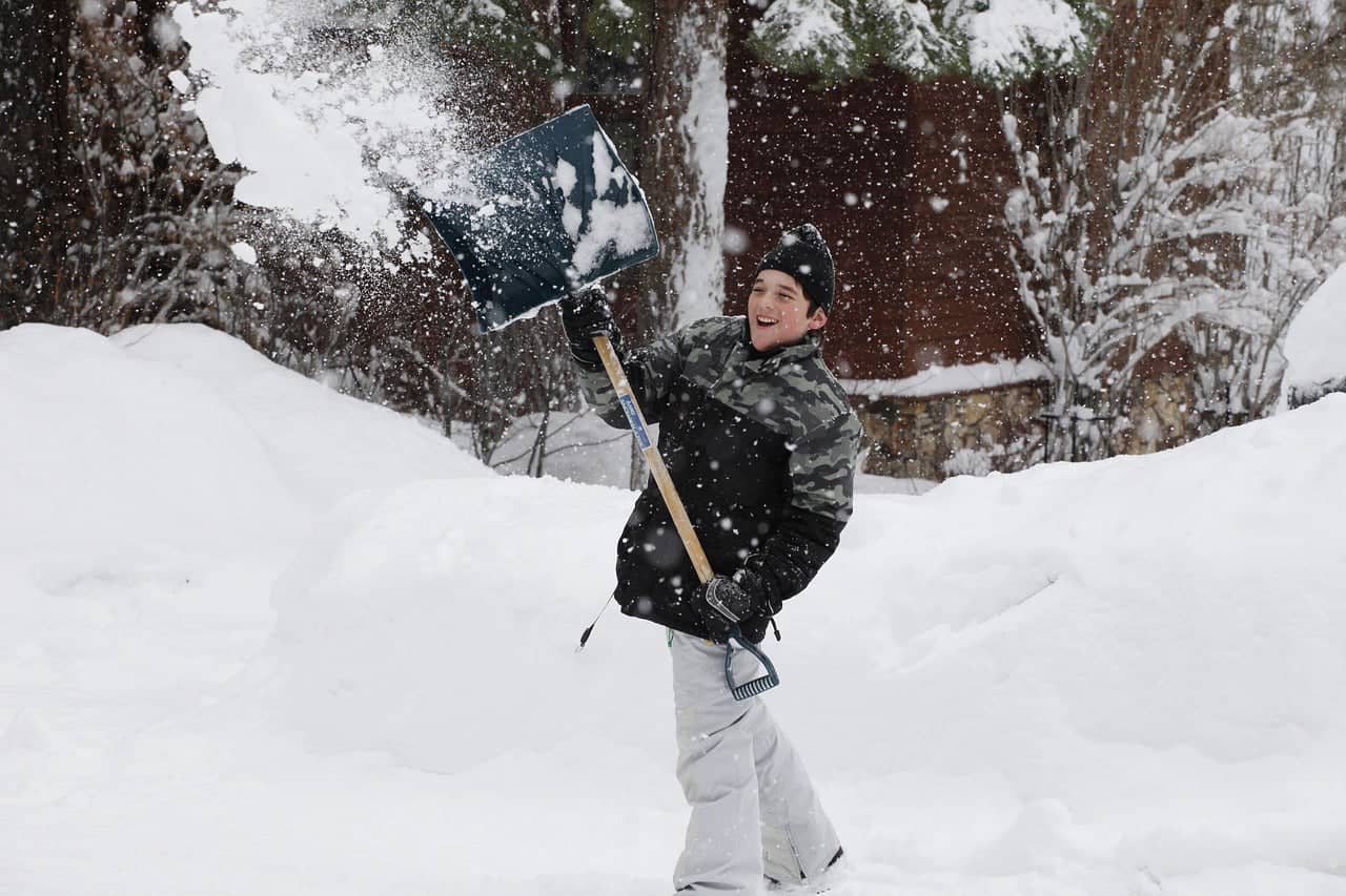 A person shoveling snow wearing winter gear, highlighting why do you need a base layer for insulation and moisture control